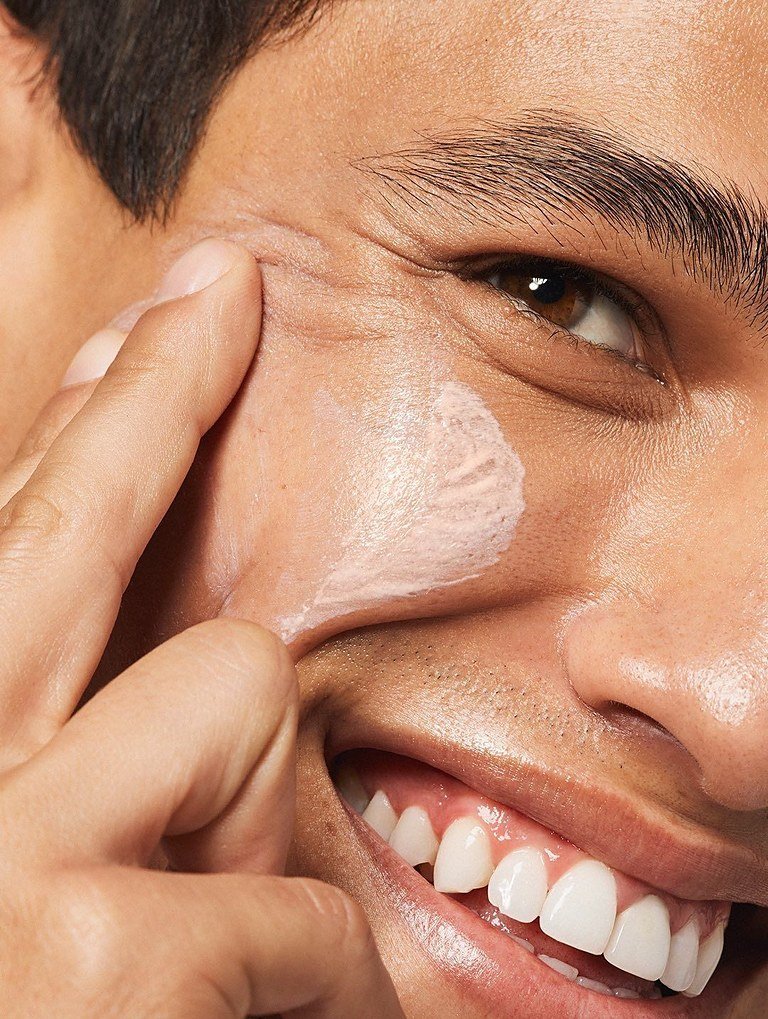 Homme qui sourit en appliquant une crème sur la joue